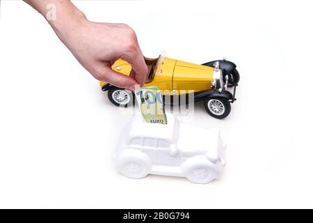La main est de saisir un billet dans la boîte à monnaie en forme de voiture en céramique avec la voiture modèle derrière. Il peut être le symbole des coûts des réparations et des investissements de la voiture. Banque D'Images