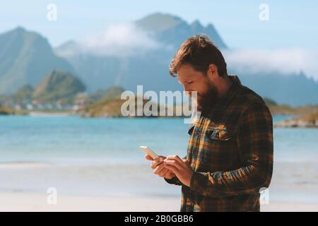 Homme utilisant smartphone marchant sur la plage technologie moderne influenceur indépendant vie vacances été mer et montagnes paysage en Norvège Banque D'Images