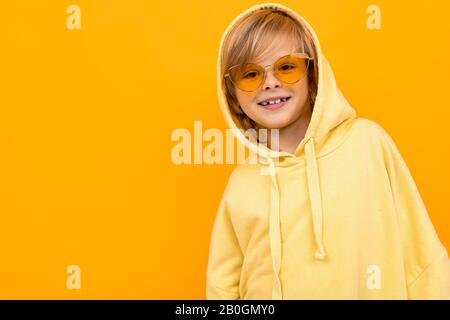 Beau garçon en jaune hoodie sourires et gestilates isolés sur fond orange Banque D'Images