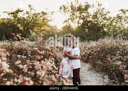 Vue centrale de frère et sœur embrassant dans le champ de fleurs rétroéclairé Banque D'Images