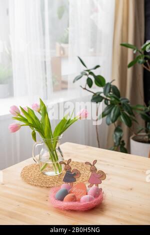 Gros plan de table en bois avec nid de Pâques rose avec œufs colorés et Carte Joyeuse de Pâques, tulipes dans le pichet sur la serviette Banque D'Images