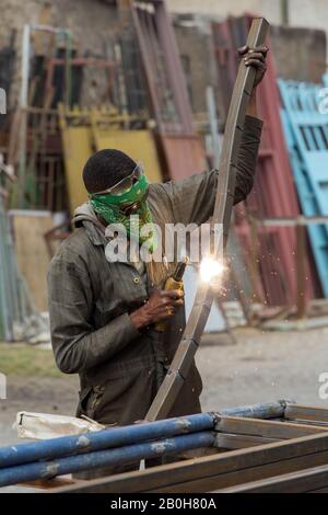 07.11.2019, Adama, Oromiyaa, Ethiopie - un serrurier soudure des portes et des grilles ensemble dans la rue à l'aide d'une machine de soudage électrique. Il porte du soleil Banque D'Images