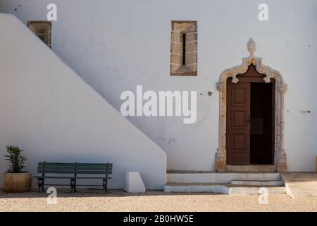 Mur latéral et entrée à l'église Igreja Matriz de Alvor. Porte ouvragée à moitié ouverte avec voûte. Ligne du mur couvrant les escaliers. Façade blanche. Alv Banque D'Images