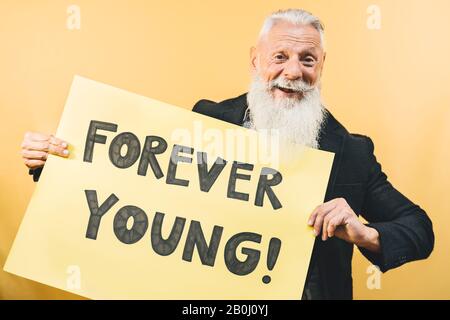 Heureux jeune jeune senior sentiment pour toujours jeune - Hipster homme mûr donnant message avec bannière jaune Banque D'Images