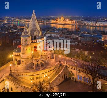 Budapest, Hongrie - vue aérienne de la tour principale de Fisherman's Bastion (Halaszbastya) avec Parlement éclairé de la Hongrie à l'heure bleue sur une trinte Banque D'Images