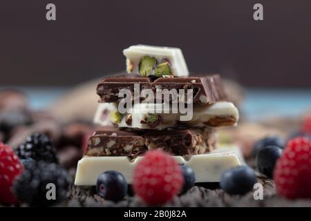 Baies forestières et chocolat sur terre de bois. Assortiment de chocolat blanc, noir et au lait avec noix au chocolat pistache. Banque D'Images