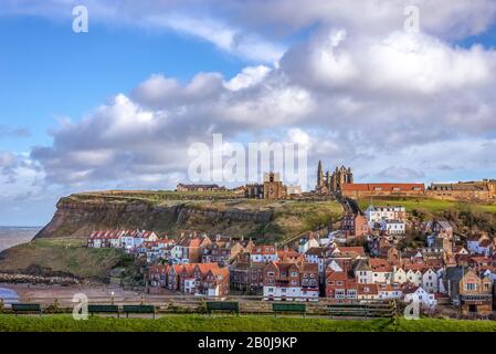 Le port extérieur de Whitby. Maisons nichées sous la falaise avec une église et l'abbaye de Whitby sur le sommet de la colline. Une ligne de bancs se trouve au premier plan. Banque D'Images