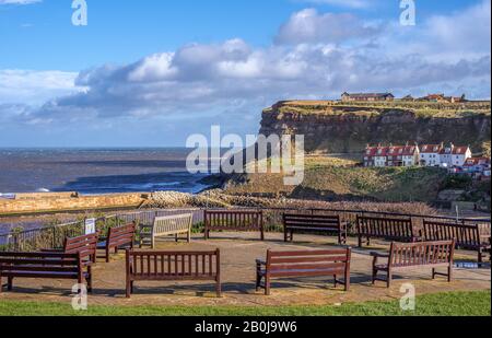 Whitby: Un certain nombre de bancs disposés en courbe sur un sommet de falaise surplombant l'entrée du port et une falaise. Un ciel nuageux est au-dessus. Banque D'Images