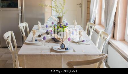 Décoration festive de table de Pâques, serviettes en forme d'oreilles de lapin, œufs de poule et de caille teints, gâteaux, violettes potées, plumes, dîner en famille o Banque D'Images
