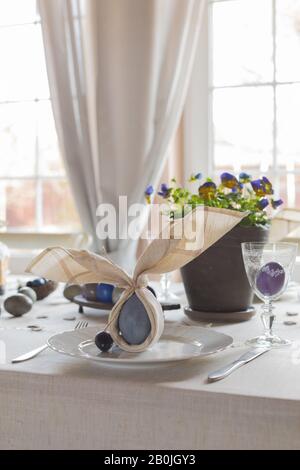 Décoration festive de table de Pâques, serviettes en forme d'oreilles de lapin, œufs de poule et de caille teints, gâteaux, violettes potées, plumes, dîner en famille o Banque D'Images