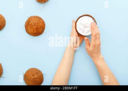 Cosmétiques biologiques à la noix de coco, crème à la noix de coco, huile, lotion pour la peau ou les cheveux dans les mains des femmes sur fond bleu pastel. Crème hydratante pour les soins de la peau Banque D'Images