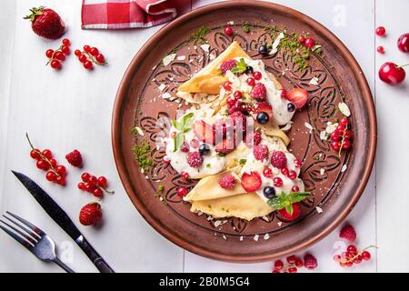 Crêpes maison avec crème aigre et baies sur fond blanc, Maslenitsa de vacances traditionnel Banque D'Images