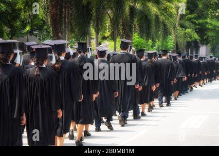 Vue arrière du groupe de diplômés universitaires en robes noires s'aligne pour le diplôme à l'université cérémonie de remise de diplômes. L'éducation Concept félicitations, stu Banque D'Images