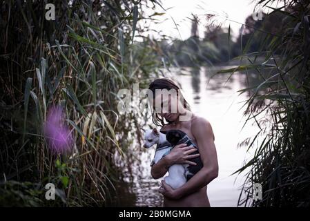 forte femme mixte de race tient deux petits chiens dans le lac naturel de berlin Banque D'Images