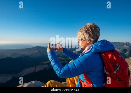 Jeune femme debout sur des rochers au sommet d'une montagne avec un téléphone portable. Banque D'Images