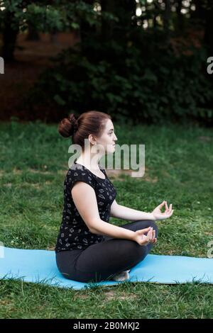 La fille détendue fait du yoga dans le parc sur la moquette Banque D'Images