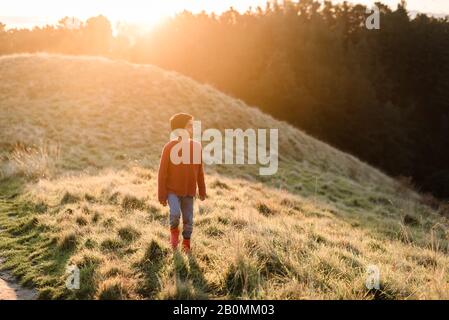 Tween garçon marchant sur une colline herbeuse au coucher du soleil Banque D'Images