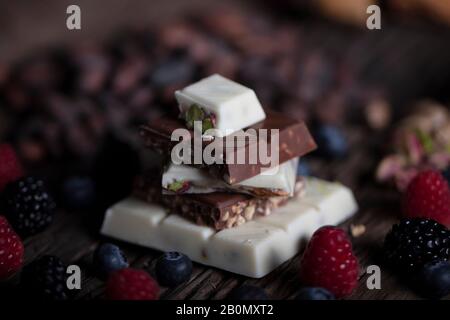 Délicieux chocolat aux baies forestières sur terre de bois. Assortiment de chocolat blanc, noir et au lait avec noix au chocolat pistache. Banque D'Images