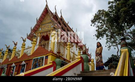 Femme à sarong tenant un chapeau devant un temple thaïlandais à Pak Nam Pran, Pranburi Thaïlande Banque D'Images