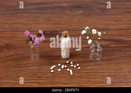 Bouteille avec pilules homéopathiques et fleurs sur fond de bois. Banque D'Images