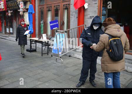 Un garde de sécurité chinois masqué vérifie la température corporelle d'un visiteur pour la prévention du nouveau coronavirus et de la pneumonie à un hutong à Beijing, C Banque D'Images