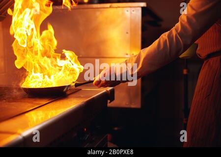 Flambe. Feu dans la poêle à frire. Chef professionnel dans une cuisine commerciale. Faites frire des aliments dans une poêle moulante sur la table de cuisson dans la cuisine extérieure Banque D'Images