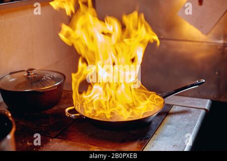 Flambe. Feu dans la poêle à frire. Chef professionnel dans une cuisine commerciale. Faites frire des aliments dans une poêle moulante sur la table de cuisson dans la cuisine extérieure Banque D'Images