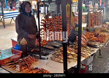 Femme vend des ailes de poulet barbecue et du poisson sur des bâtons, marché alimentaire nocturne du Ramadan et bazar, Kota Kinabalu, Sabah, Bornéo, Malaisie Banque D'Images