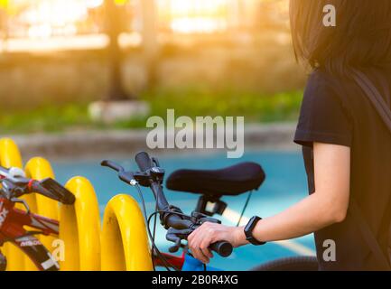 Systèmes de partage de vélos. Location de vélos pour affaires. Une femme asiatique porte un groupe intelligent qui va faire du vélo pour visiter la ville à la station de stationnement pour vélo. Eco Banque D'Images