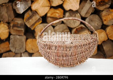 panier en bois en osier. contenant vintage de brindilles et branches sur neige blanche. sur fond de grumes en bois Banque D'Images