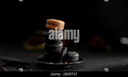 Vue rapprochée des macarons français de couleur sombre sur la plaque noire sur le fond sombre de la table Banque D'Images