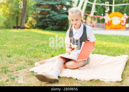 Une écolière en uniforme fait des devoirs dans le parc. L'enfant étudie à l'extérieur. Tutoriel à distance. Fille tenant une pomme dans la main Banque D'Images