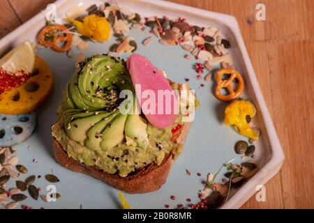 Vue de dessus du toast avec demi-avocat sur une base de feta et d'avocat brouillés, tomate et huile râpée servie dans une plaque octogonale avec fruits secs et Banque D'Images