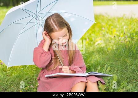 enfant lisant un livre. petite fille sous un parapluie se trouve sur l'herbe verte pendant une journée ensoleillée Banque D'Images