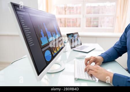 Vue Arrière D'Un Homme D'Affaires Analysant Les Graphiques Sur Ordinateur Sur Le Lieu De Travail Banque D'Images