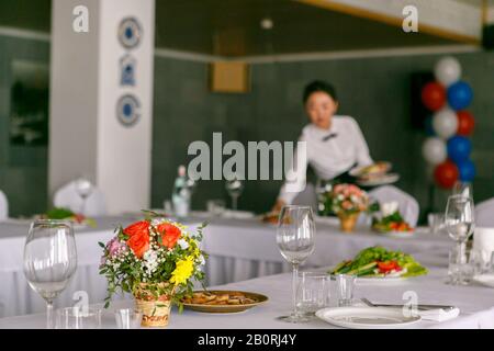 Une table de restaurant avec la serveuse sert la table de banquet dans l'arrière-plan Banque D'Images