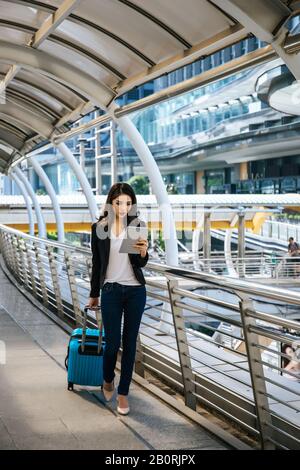 Belle jeune femme d'affaires marchant à l'extérieur de la station de transport en commun. Voyageur d'affaires avec valise sur le chemin de l'aéroport. Banque D'Images