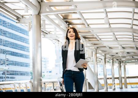 Belle jeune femme d'affaires marchant à l'extérieur de la station de transport en commun. Voyageur d'affaires avec valise sur le chemin de l'aéroport. Banque D'Images