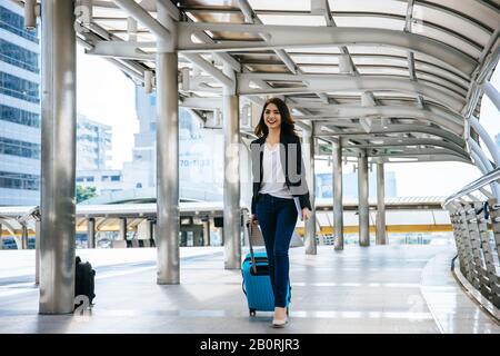 Belle jeune femme d'affaires marchant à l'extérieur de la station de transport en commun. Voyageur d'affaires avec valise sur le chemin de l'aéroport. Banque D'Images