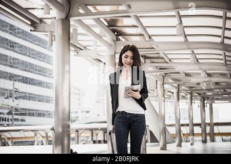 Belle jeune femme d'affaires marchant à l'extérieur de la station de transport en commun. Voyageur d'affaires avec valise sur le chemin de l'aéroport. Banque D'Images