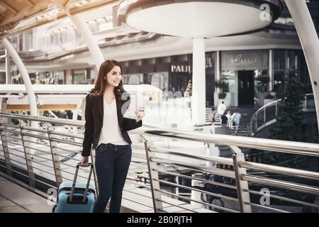 Belle jeune femme d'affaires marchant à l'extérieur de la station de transport en commun. Voyageur d'affaires avec valise sur le chemin de l'aéroport. Banque D'Images