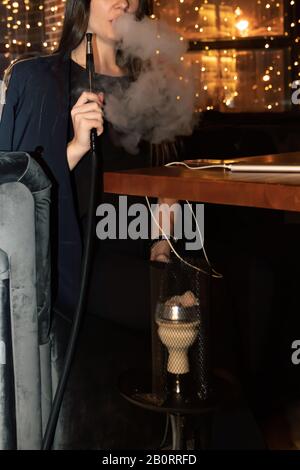 Une fille fume un tuyau de hookah dans un café de nuit. L'intérieur d'un café typique du hookah dans la ville, où les amis se réunissent le soir pour se détendre. La vie urbaine Banque D'Images