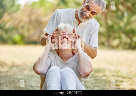 Senior tient les yeux de la femme derrière dans le jardin en été Banque D'Images