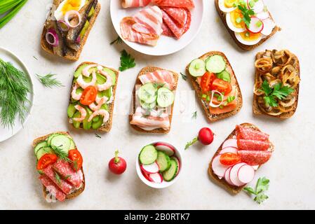 Ensemble de différents sandwichs avec viande, légumes, fruits de mer. Assortiment de sandwichs ouverts sur fond de pierre légère. En-cas savoureux et sains. Vue sur le dessus, plat l Banque D'Images