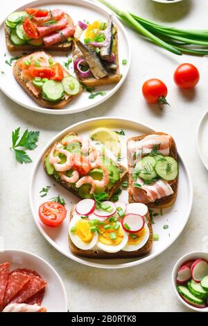 Ensemble de différents sandwichs avec viande, légumes, fruits de mer. Assortiment de sandwichs ouverts sur fond de pierre légère. En-cas savoureux et sains. Banque D'Images