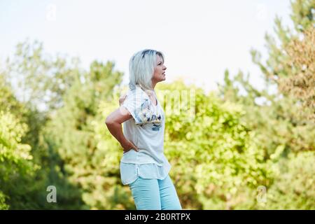 La vieille femme dans la nature a la douleur de dos et la maintient dans le dos Banque D'Images