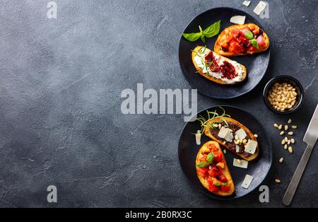 Bruschetta avec tomates, fromage et tapenade d'olive sur des assiettes noires. Fond gris ardoise. Vue de dessus. Espace de copie. Banque D'Images