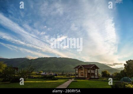 Ciel bleu, nuages, aube, herbe verte avec chalet touristique en bois trottoirs, tentes touristiques, et montagnes cultivées de forêt sur l'arrière-plan et lumineux Banque D'Images