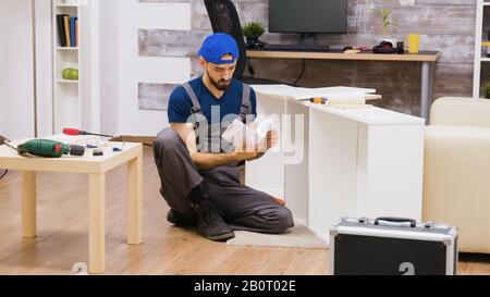 Zoom avant de l'homme en salopette assemble une étagère et des instructions de lecture. Banque D'Images