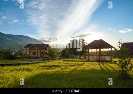 Champ vert avec de petits arbres, chalet touristique, belvédères, trottoir en bois, tentes touristiques, et montagnes cultivées en forêt sur le fond et cl bleue Banque D'Images